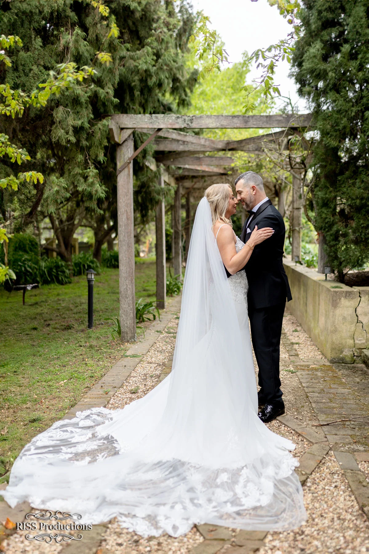 Affy and Glen embracing beneath a garden pergola at Fitzroy Inn, Mittagong