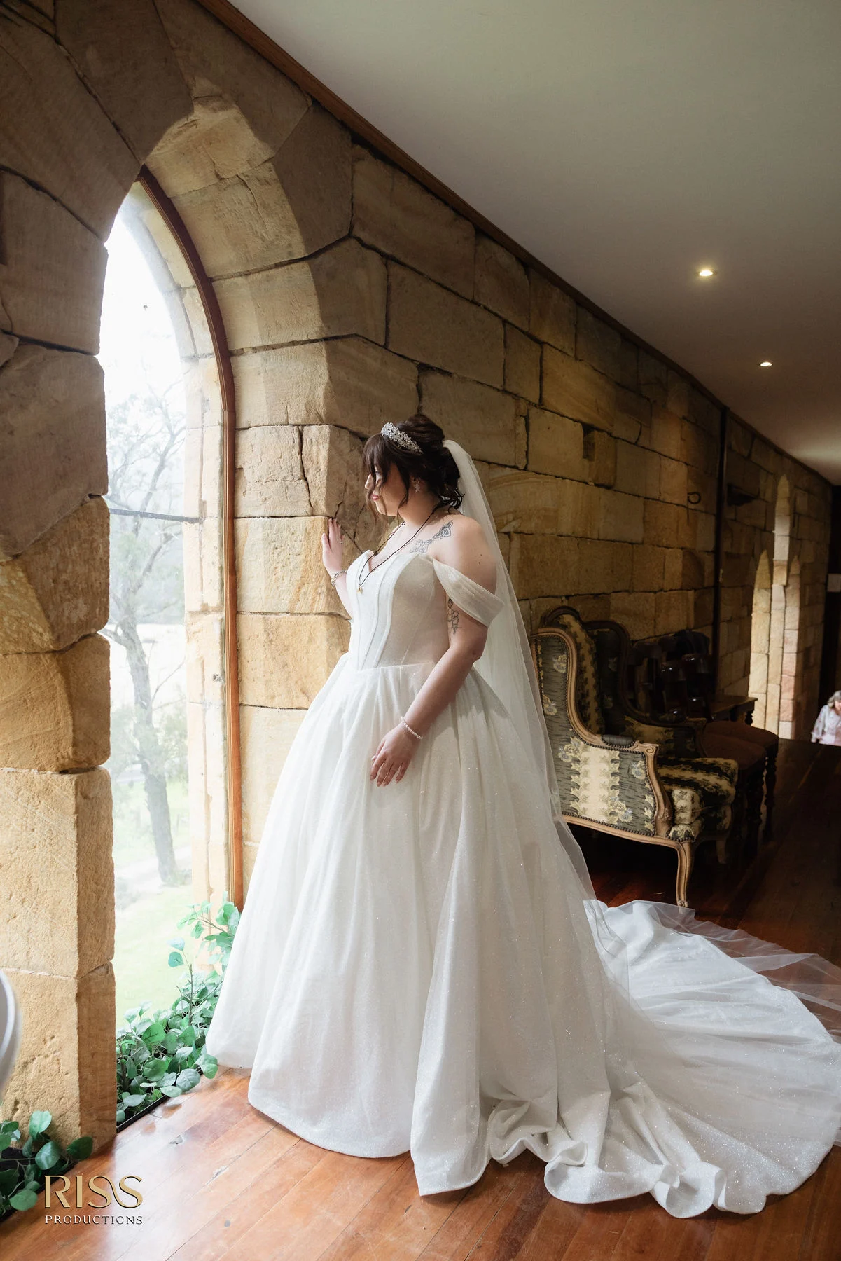Bride Erin in her wedding gown beside arched sandstone windows at St Joseph's Guest House