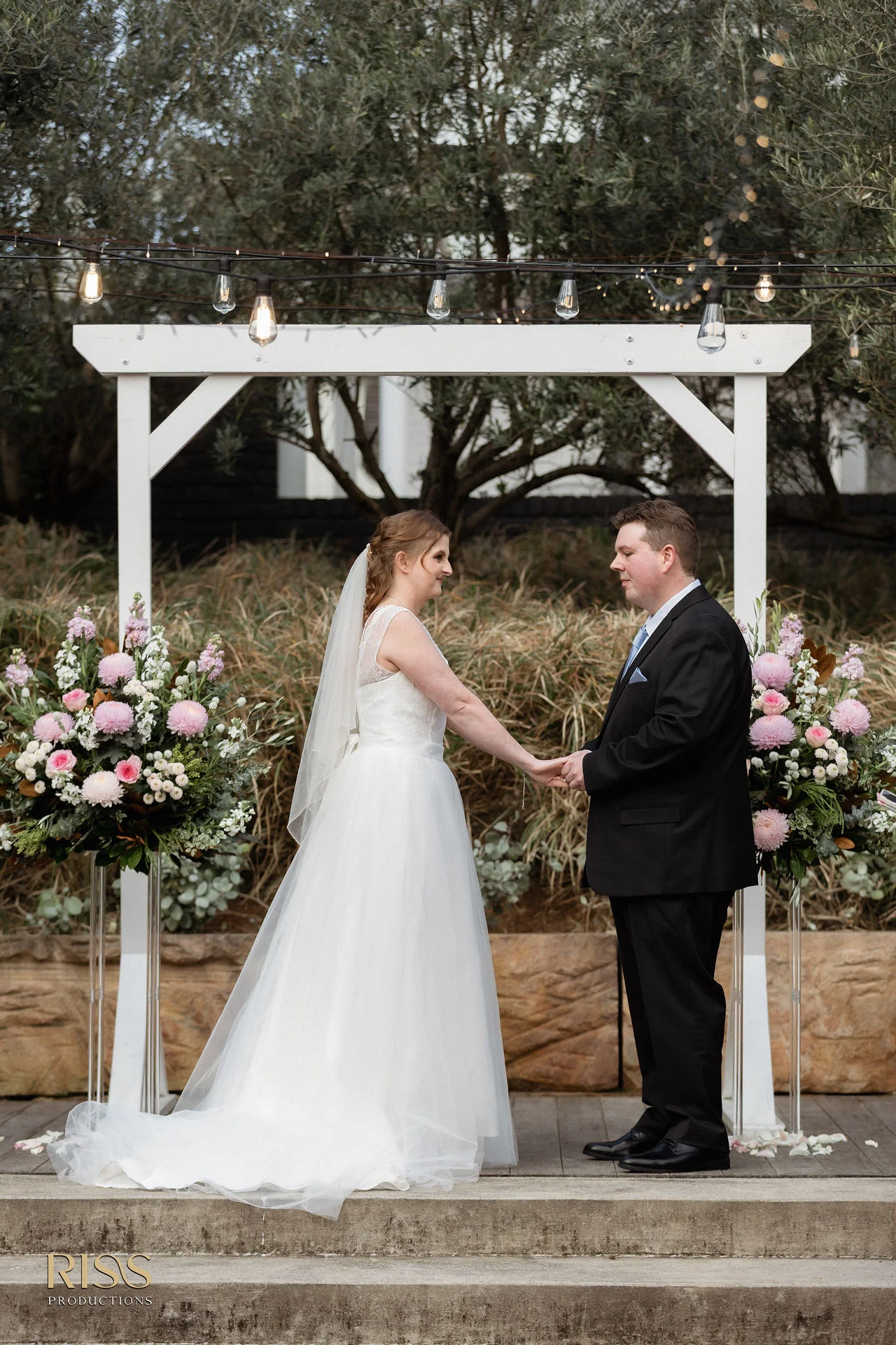 Lauren and Ryan exchanging vows under a floral arbour at The Olive Grove