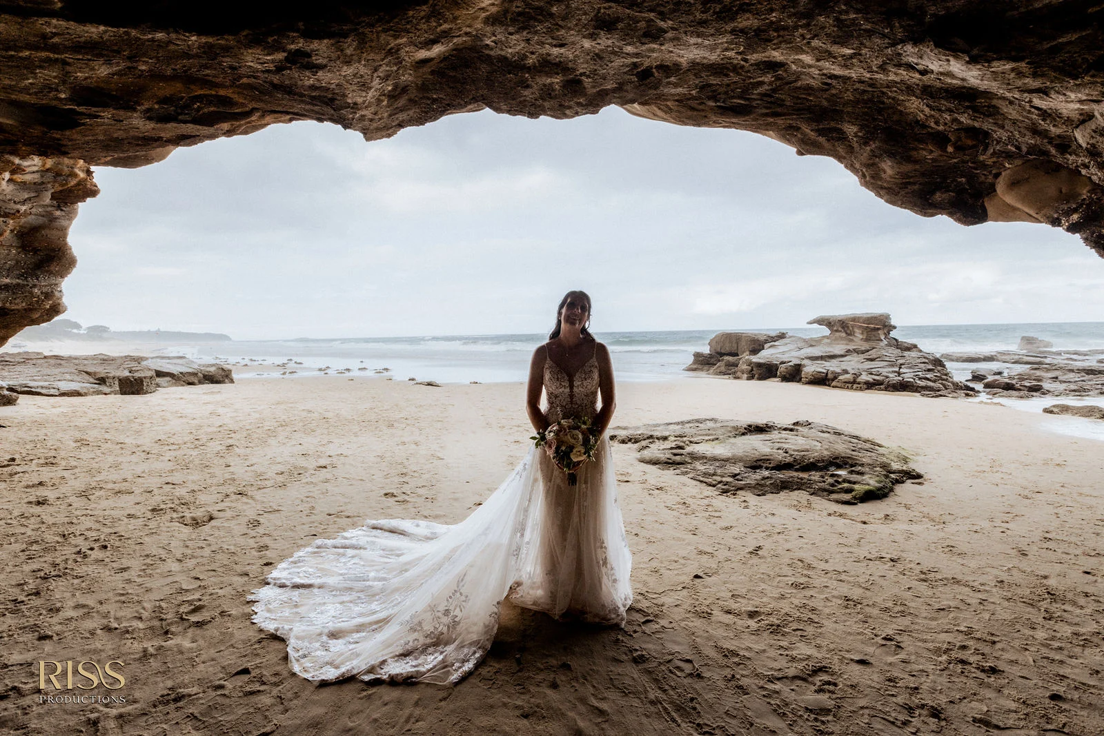 Bride standing in a sea cave looking out to Caves Beach