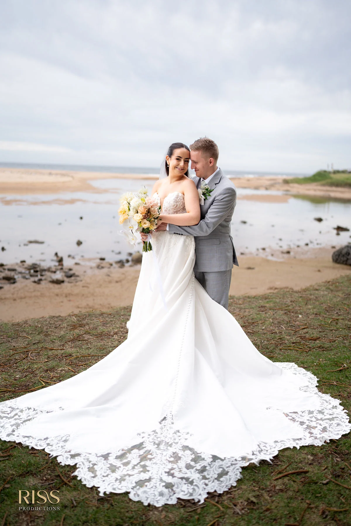 Meghan and Lachlan with her long lace train by the water in Wollongong
